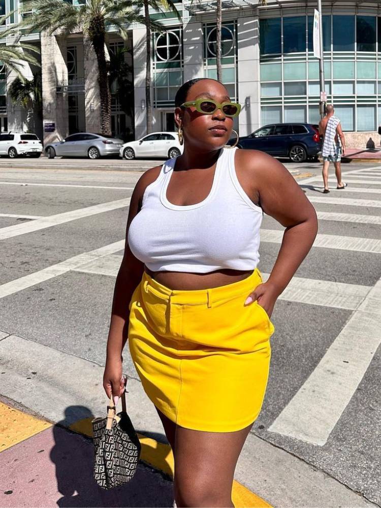 mulher usando regata branca com saia amarela e bolsa preta estampada
