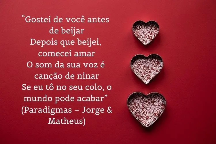 Cartão virtual de fundo vermelho com corações e frase “Gostei de você antes de beijar / Depois que beijei, comecei amar / O som da sua voz é canção de ninar / Se eu tô no seu colo, o mundo pode acabar” (Paradigmas – Jorge & Matheus)