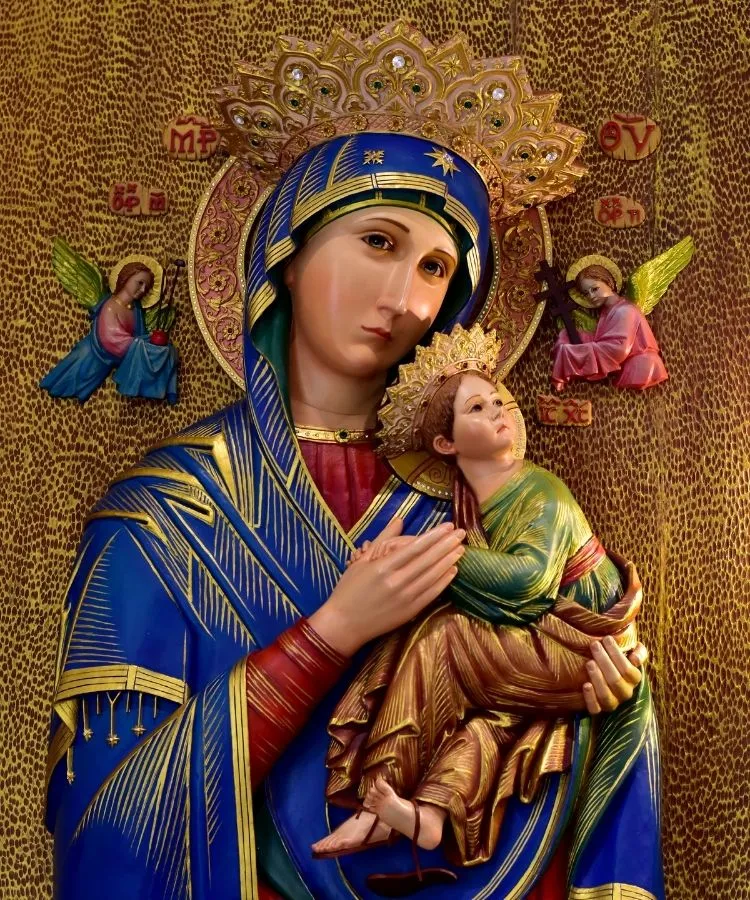 Imagem de Nossa Senhora do Perpétuo Socorro, em manto azul com detalhes dourados, segurando o Menino Jesus. Eles possuem coroas ornamentadas. Dois anjos ladeiam, com símbolos sagrados, sobre fundo dourado detalhado e inscrições em vermelho.
