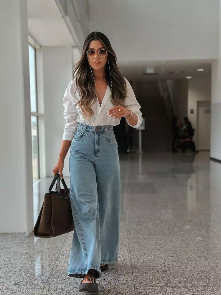 Mulher de pele clara com camisa branca e calça jeans pantalona cintura alta