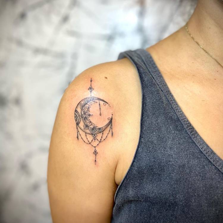 Mulher de pele clara e regata cinza com tatuagem de lua e ornamentos sombreada