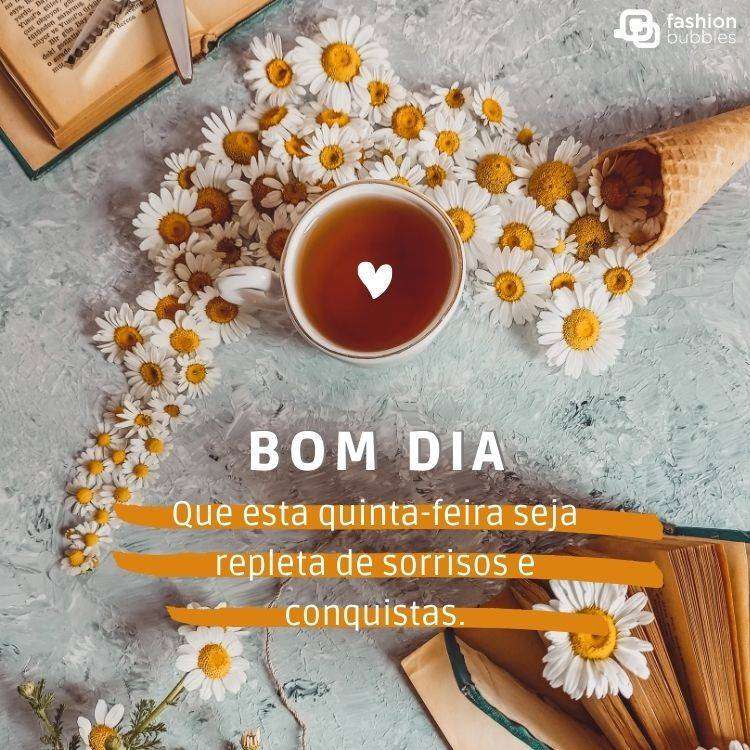 Foto de mesa com margaridas e xícara de chá, com frase "Bom dia! Que esta quinta-feira seja repleta de sorrisos e conquistas."