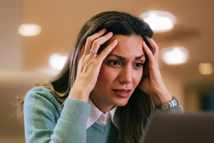 Mulher com expressão de frustração, mãos na cabeça, olhando para um laptop. A imagem reflete emoções intensas, ideal para ilustrar temas como choque cultural e psicanálise.





