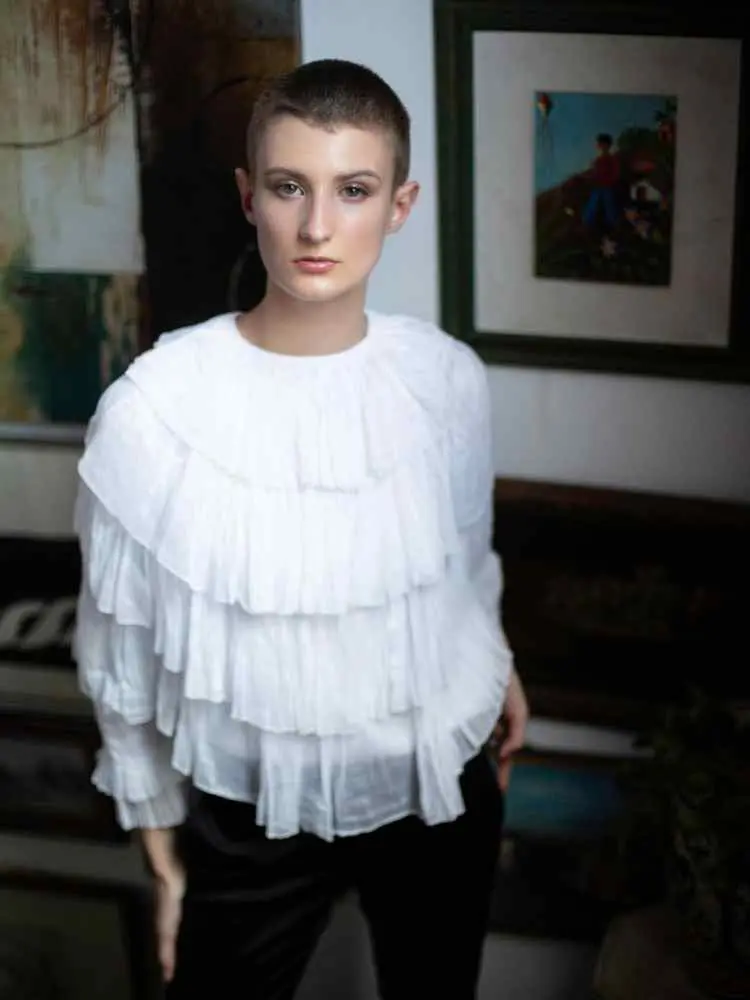 Mulher não-modelo com mais de 30 anos em ensaio fotográfico, usando blusa de babados branca + calça preta 