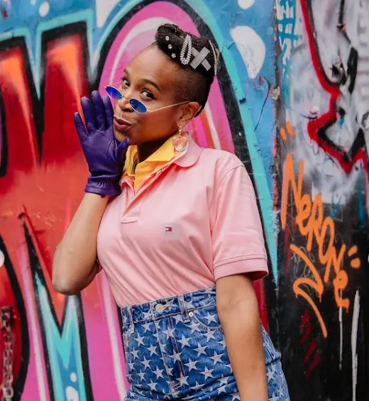 Looks Karol Conka com óculos oval azul, clips de cabelo, polo e saia jeans 