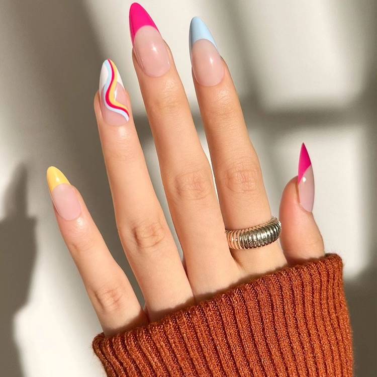 Mão com unhas arco-íris LGBTQIA+: Polegar: nude com francesinha pink Indicador: nude com francesinha azul Médio: nude com francesinha pink Anelar: nude com branca e arco-íris curvado Mínimo nude com francesinha amarela