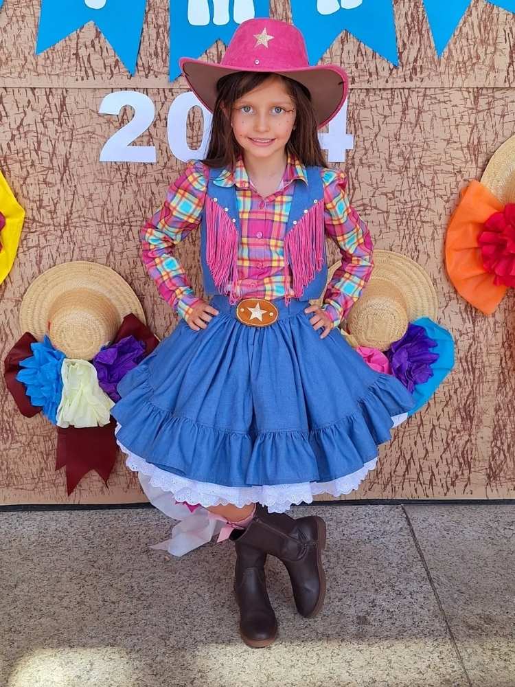 Menina de pele clara com vestido azul com franjas rosas e chapéu country 