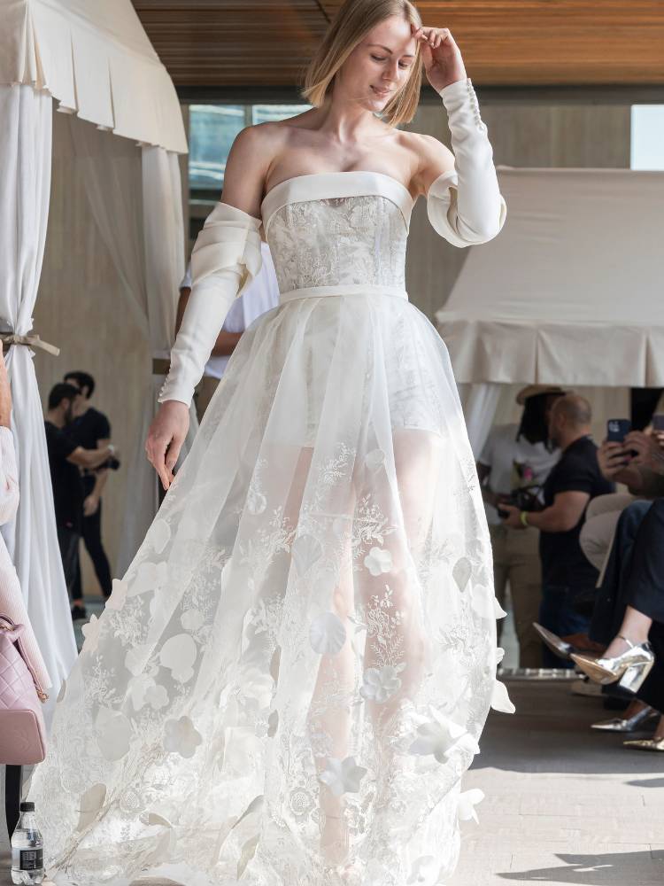 Mulher de pele clara usando vestido de noiva sem alça, transparência na saia e luvas brancas