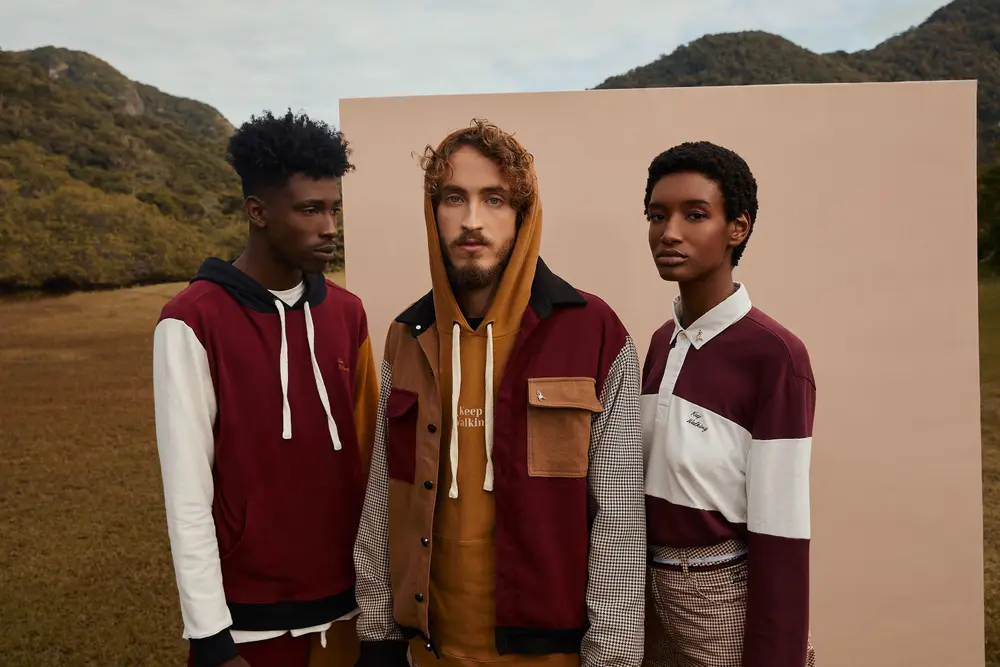 Três modelos em pé juntos, usando roupas de cores mostarda, vinho, branco e azul marinho