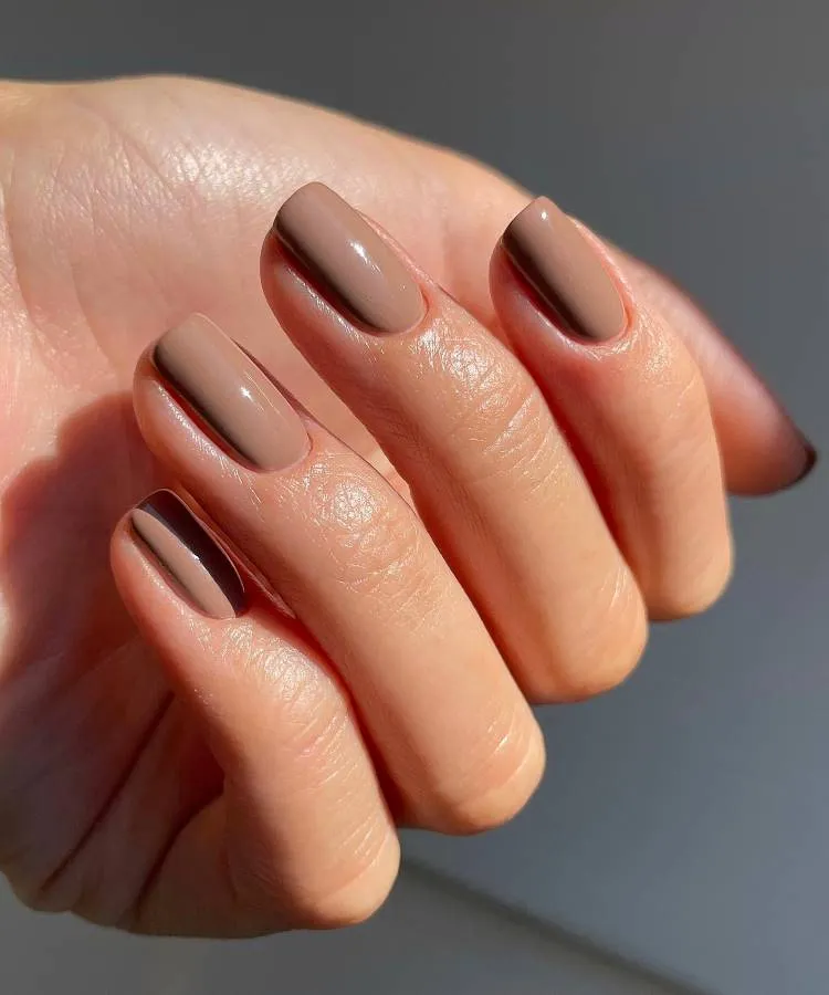 Mão feminina com unhas no formato quadrado com as pontas arredondadas na esmaltação marrom em fundo claro
