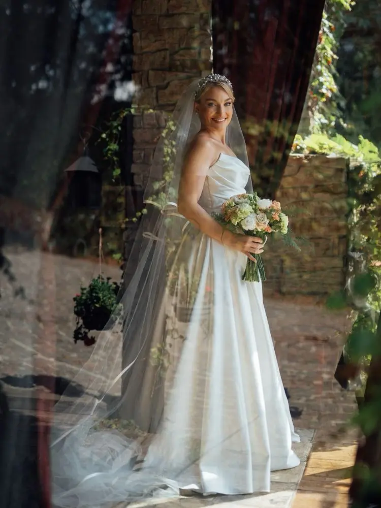Mulher de pele clara em chateau usando vestido encorpado de noiva, véu e buquê