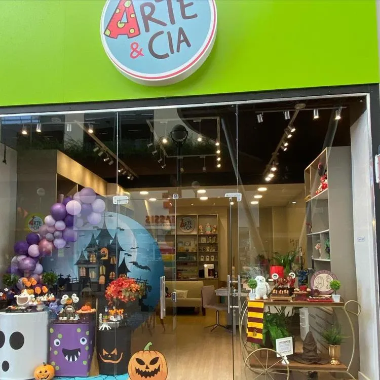 Vitrine com painel de halloween à esquerda, com enfeites de mesa e bexigas roxas. Do lado direito, carrinho com itens decorativos de Harry Potter 