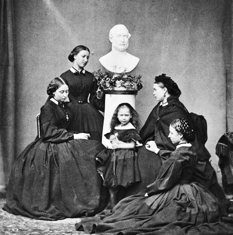 Foto em preto e branco das cinco filhas da Rainha Vitória, Alice, Helena, Beatrice, Victoria e Louise, todas com vestidos pretos Foto das cinco filhas da Rainha Vitória, Alice, Helena, Beatrice, Victoria e Louise.
