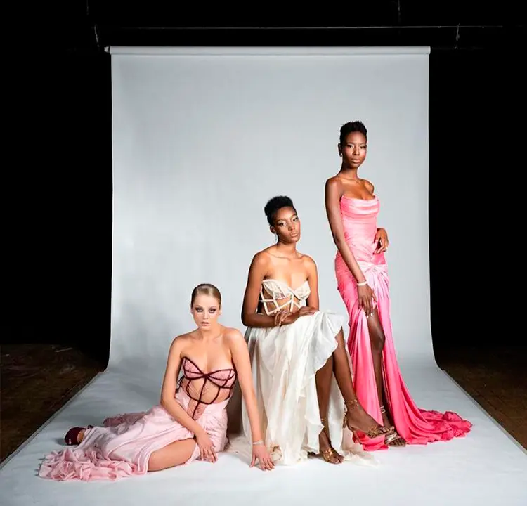 Três modelos com vestidos rosa claro, branco e rosa choque.
