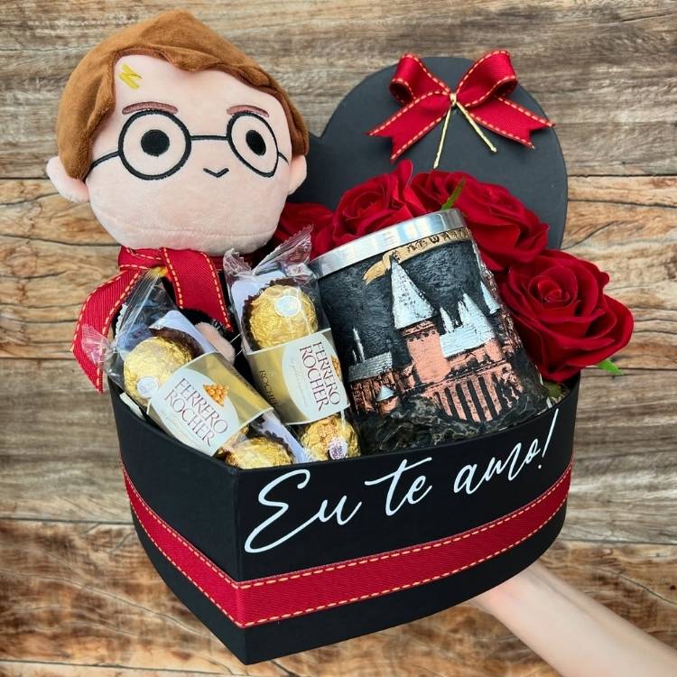 Caixa preta em formato de coração escrito "eu te amo", dentro com flores, bombons, lata de Hogwarts e pelúcia do Harry Potter 