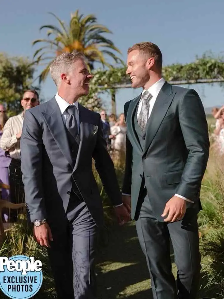 Noivos Colton Underwood e Jordan C. Brown se casando. Eles usam ternos cinza e verde-escuro.