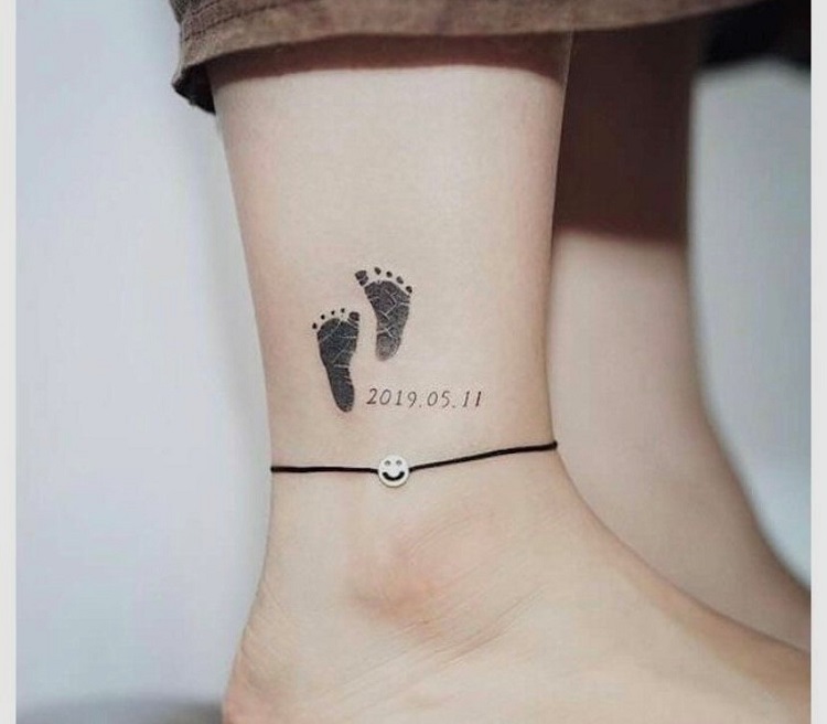 Tatuagem em homenagem a filho com dois pés e a data no tornozelo