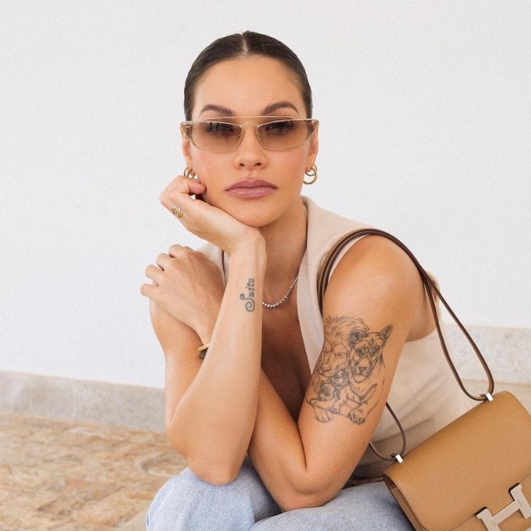 Andressa Suita de óculos de sol, regata bege e calça jeans, com tatuagem de família de leões no braço