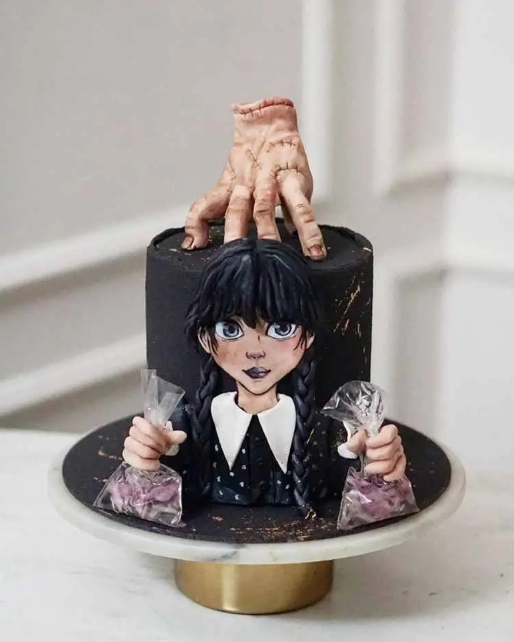 bolo preto com imagem da wandinha na frente e escultura de mão em cima