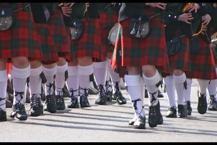 Pernas de escoceses com kilt em tartã, meias brancas e sapatos pretos 
