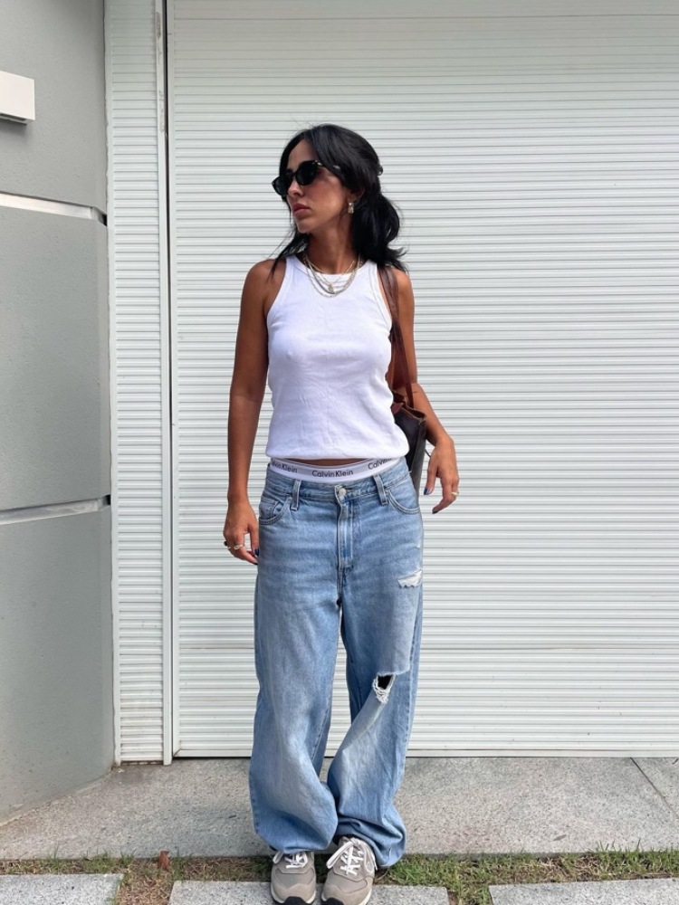 mulher usando regata branca, com calça jeans reta, tênis cinza e óculos de sol