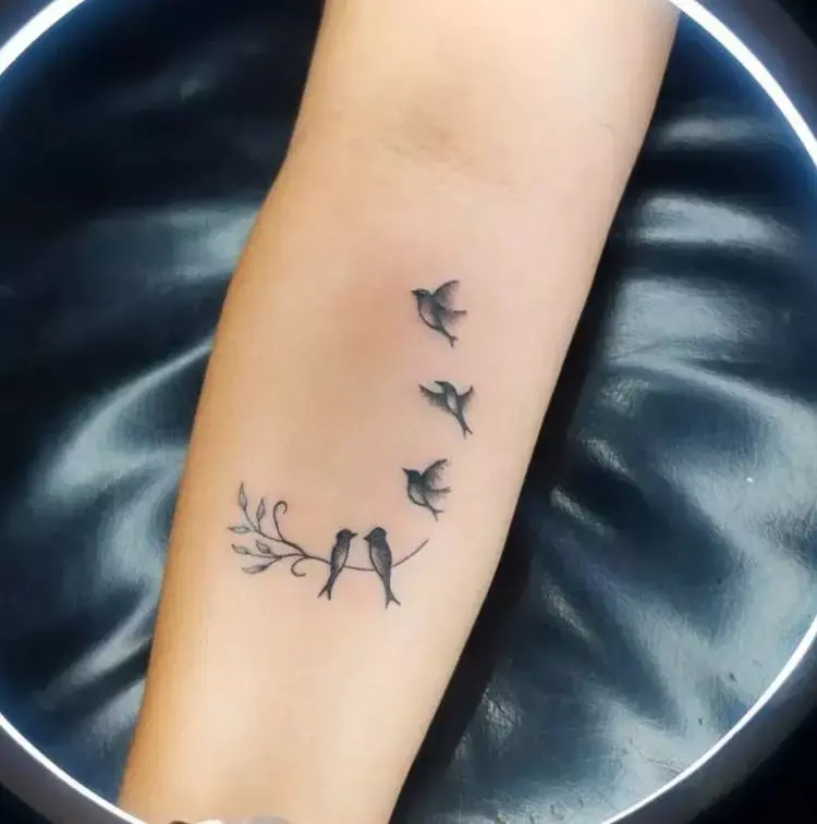 Tatuagem feminina no antebraço de pássaros voando e em galho