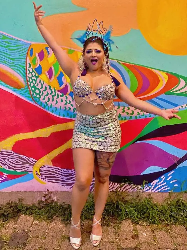 Mulher de pele clara usando top com conchas e miçangas azuis e saia que imita escama de peixe