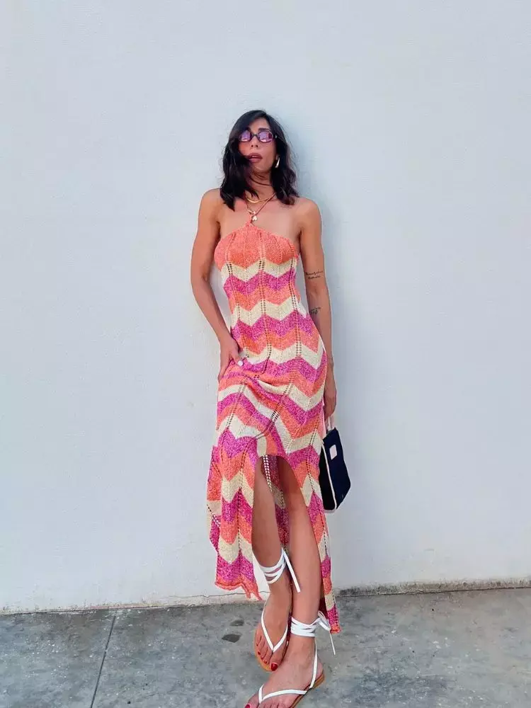 Mulher de pele clara em parede branca usando vestido de crochê geométrico rosa, salmão, lilás, entre outras cores