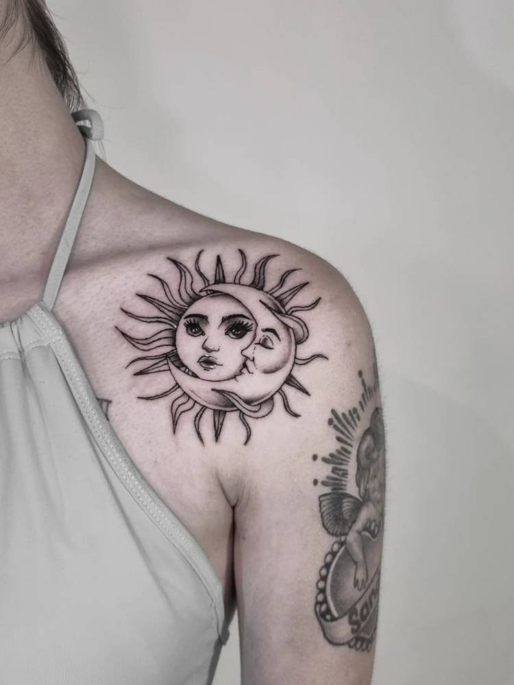 Mulher de pele clara usando blusa verde e com tatuagem de sol e lua em preto e traços grossos no ombro estilo black work