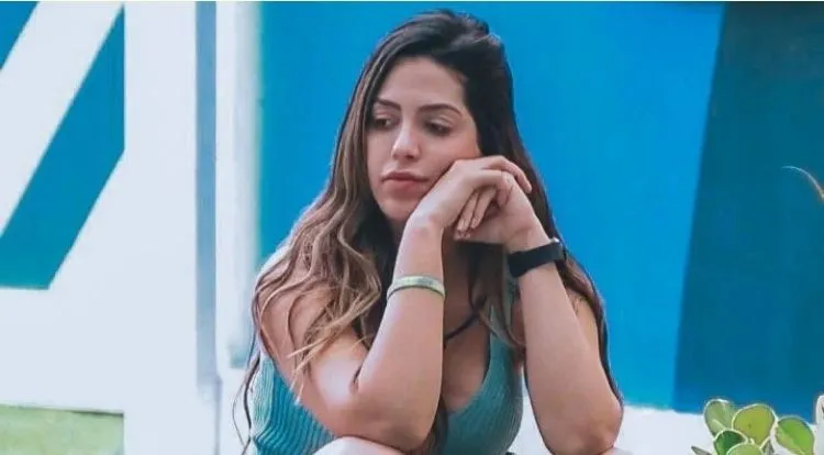 Laís Caldas usando regata azul, com maõs no rosto e expressão pensativa 
