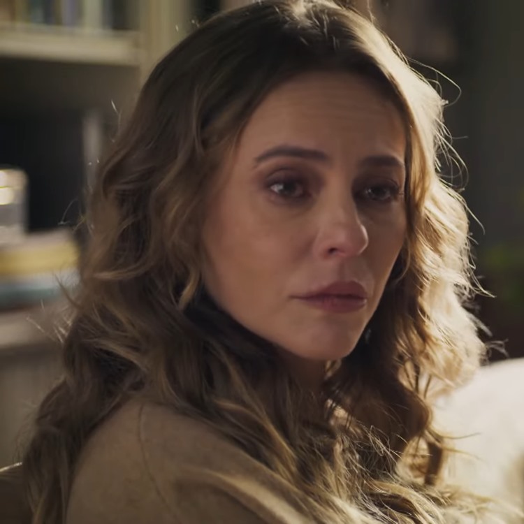 Paolla Oliveira como Heleninha mostra cortes de cabelo de Vale Tudo. Mulher de cabelos loiros ondulados e expressão triste, com olhos marejados. Veste blusa bege em ambiente interno com luz suave, fundo desfocado de estante com livros, transmitindo um momento de emoção e contemplação.





