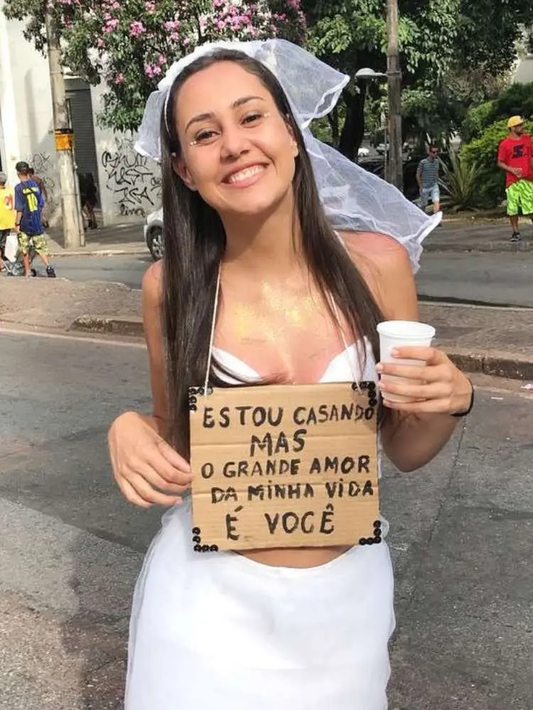 Mulher de pele clara usando fantasia d enoiva e placa escrito "estou casando mas o grande amor da minha vida é você"