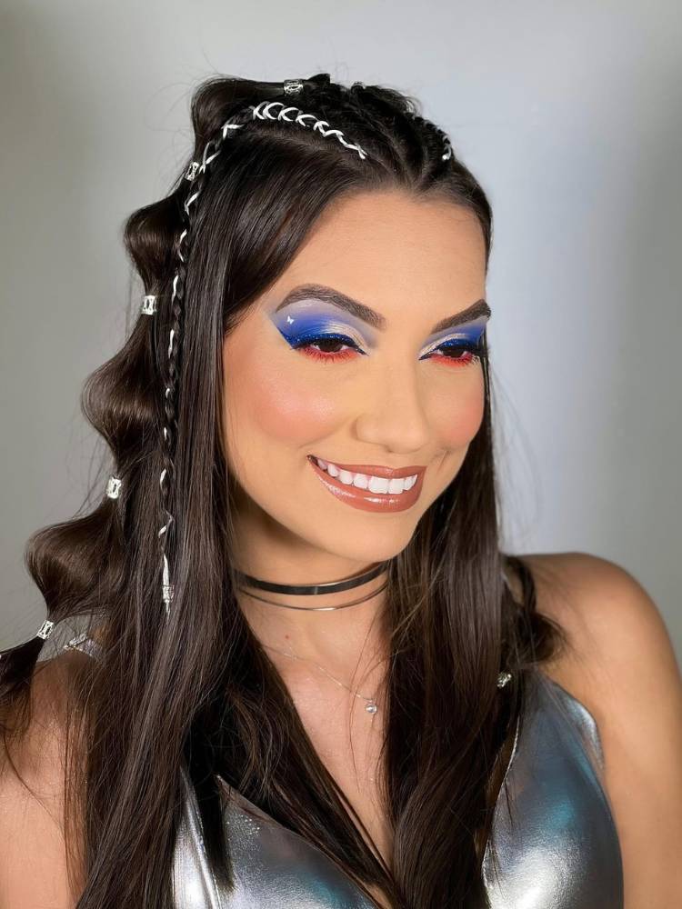 Mulher de pele clara e cabelos escuros, usando maquiagem de sombra branca, azul e vermelha. 