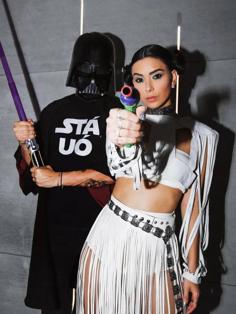 Casal de influenciadores Rica de Marré e Adrão Meron fantasiados de Star Wars para o Halloween. Ele usa traje do Darth Vader e sabe de luz roxo e ela usa visual da Leia com arma roxa 
