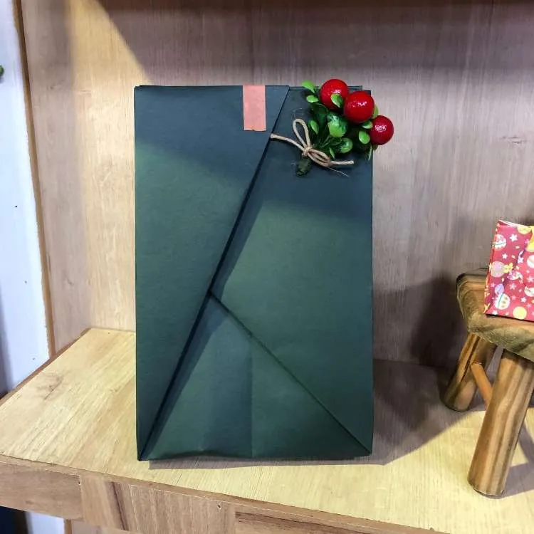Embrulho de Natal em verde feito com a técnica de origami e enfeitado com flor vermelha.