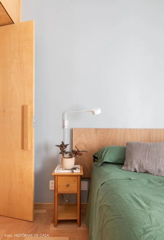 Quarto com parede cinza, chão de madeira, cabeceira de painel ripado e cama com lençóis verdes