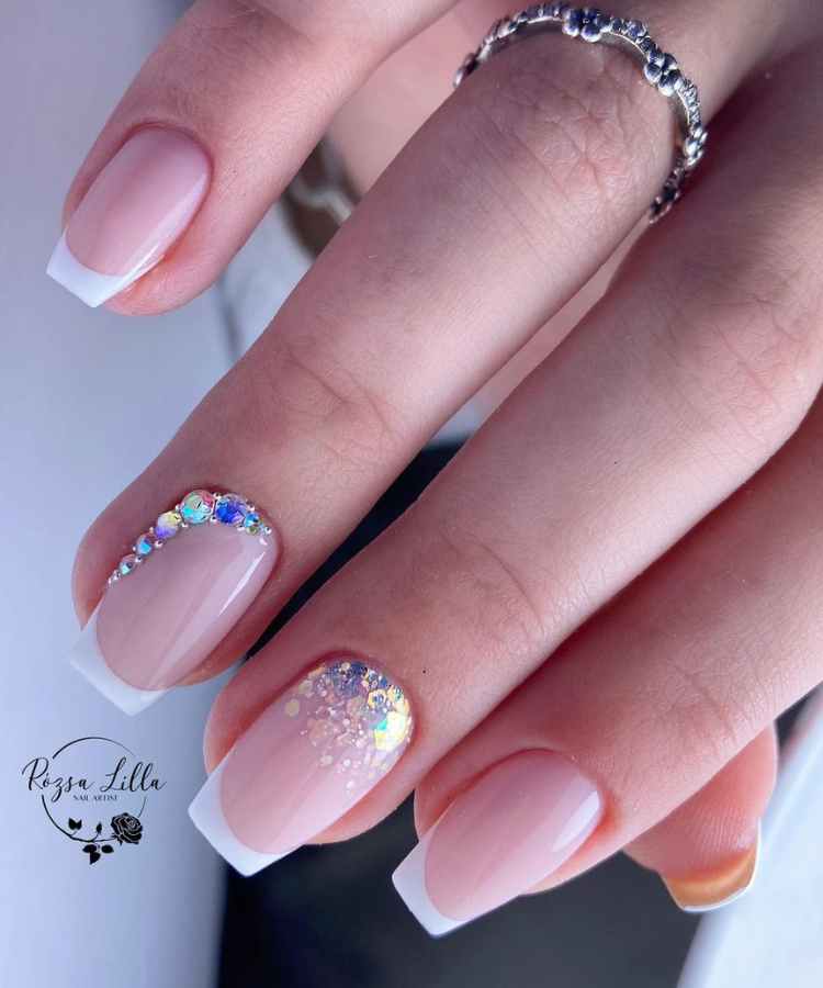 Pessoa de pele clara com unha quadrada curta e francesinha branca com glitter e pedraria 