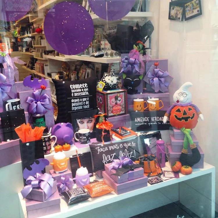 Vitrine em tons de roxo, com almofadas, pelúcias de Halloween, itens laranjas, pelúcia de gato preto, etc 
