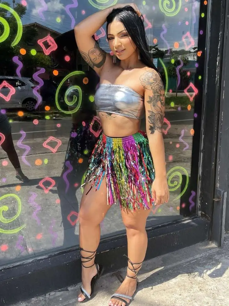 Mulher de pele clara usando tube top prata e saia de franjas coloridas