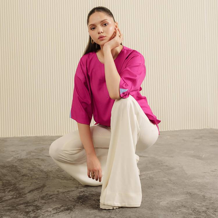 Mulher posa em fundo minimalista, usando blusa de manga larga fúcsia e calça de alfaiataria branca com corte amplo. Look casual e moderno, ideal para looks de trabalho que unem conforto e estilo. Cabelo preso e acessórios discretos.





