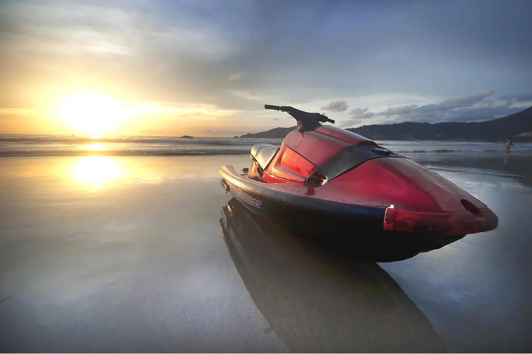 Imagem de um Jet Ski preto e vermelho estacionado em uma praia durante o pôr do sol Imagem de um Jet Ski preto e vermelho estacionado em uma praia durante o pôr do sol.