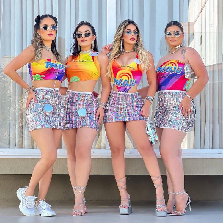 Quatro mulheres de pele clara usando saias coloridas e o mesmo abadá colorido, porém com customizações diferentes. 