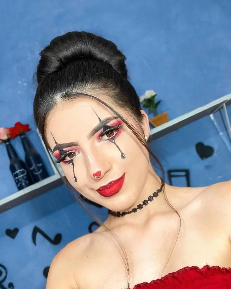 Mulher de pele clara usando maquiagem de palhaço com coração no nariz e batom vermelho