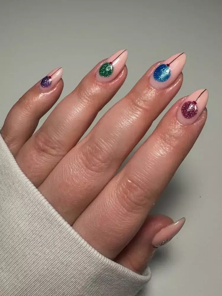 Mão de pele clara com unha almond com base bege e cada unha com bola de árvore de natal de uma com com glitter