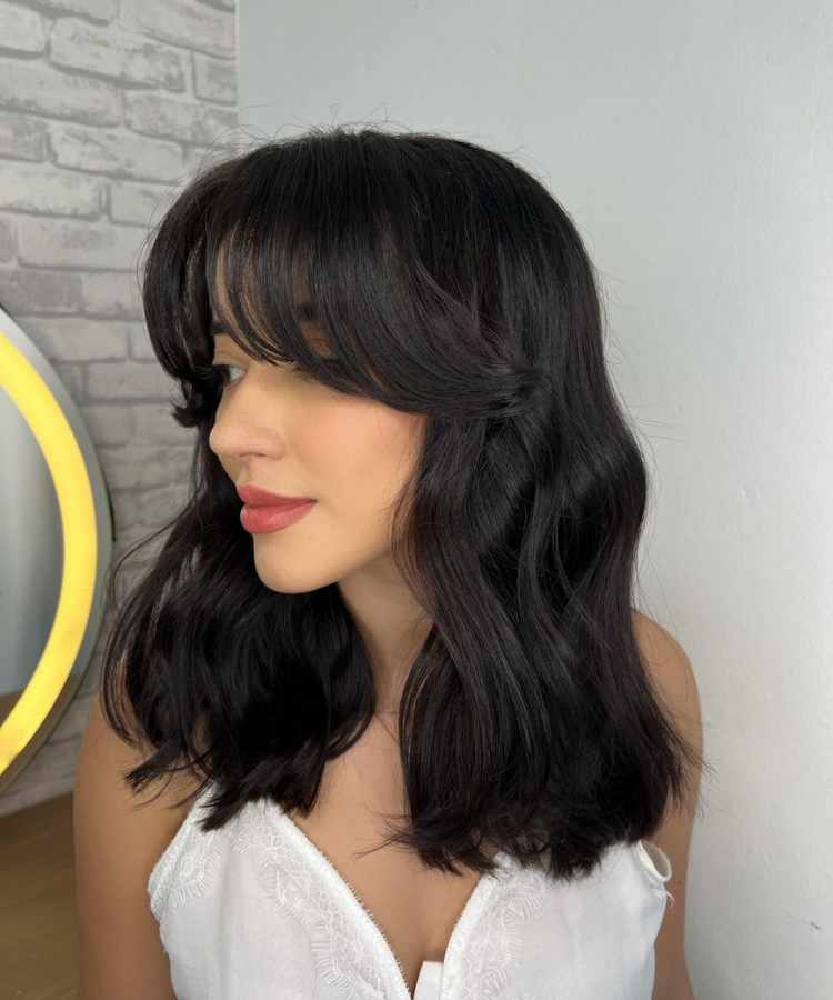 Corte de cabelo médio com franja curtain bangs.