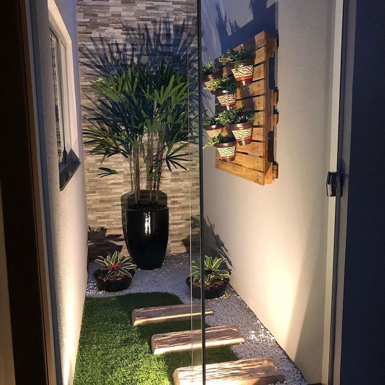 Jardim de inverno iluminado, com pallet na parede e vasos de diferentes tamanhos 
