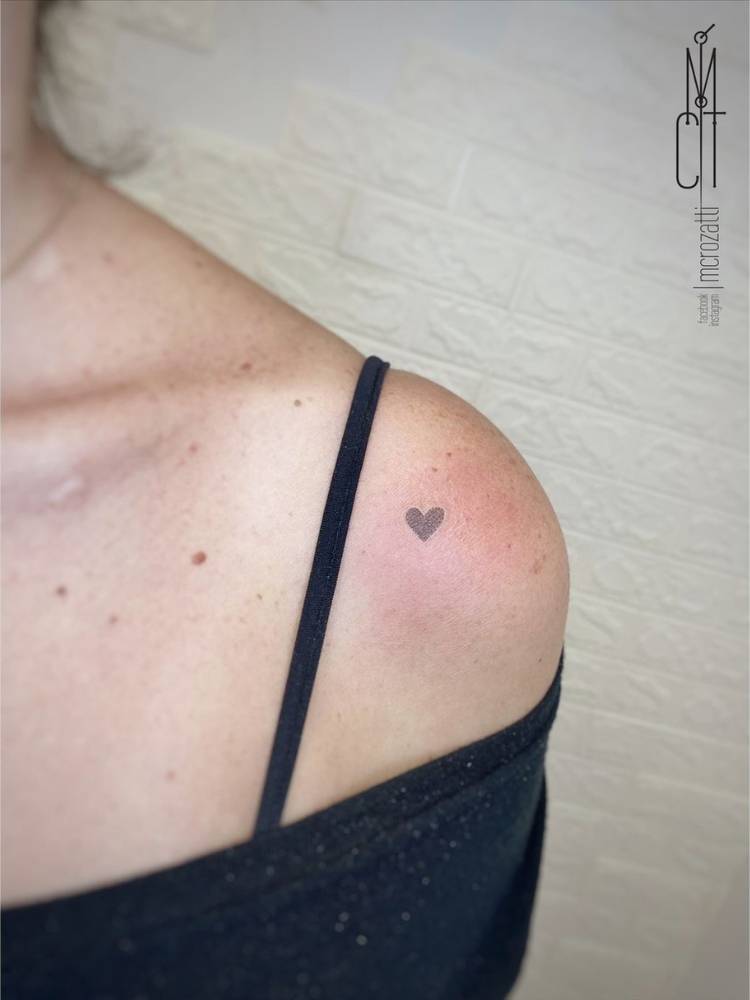 Mulher de blusa preta no ombro e sutiã preto com tatuagem de mini coração sombreado no ombro