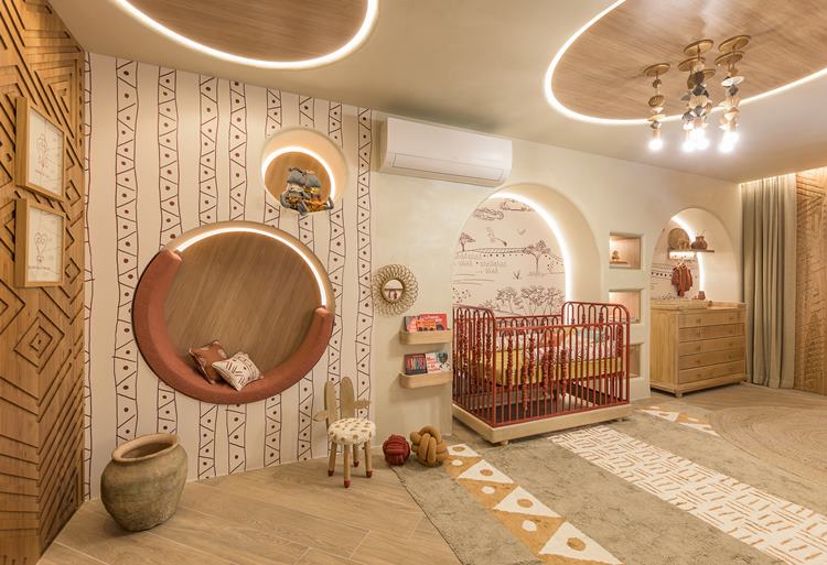 A imagem mostra um quarto infantil bem iluminado com decoração temática tribal. Inclui uma cama com grade, tapetes geométricos, espelhos redondos e iluminação embutida no teto. As paredes têm desenhos de flechas e tendas.

