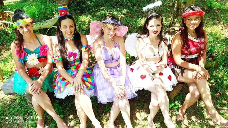 Foto de mulheres no gramado fantasiadas de flores, palhaço, fada, cupido e moana