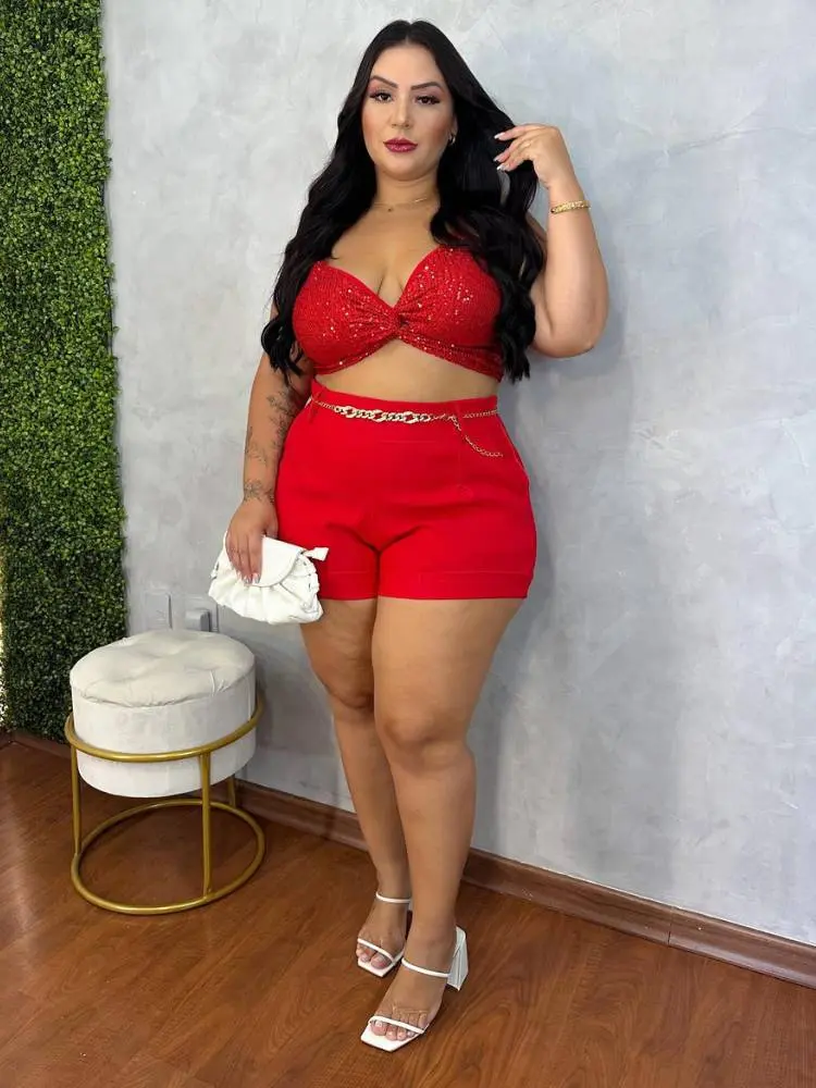 Mulher de pele clara e cabelo escuro usando top e shorts vermelhos, além de uma bolsa branca.